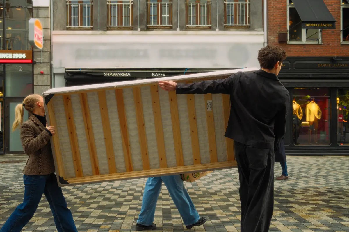 two people carrying a box spring down a sidewalk